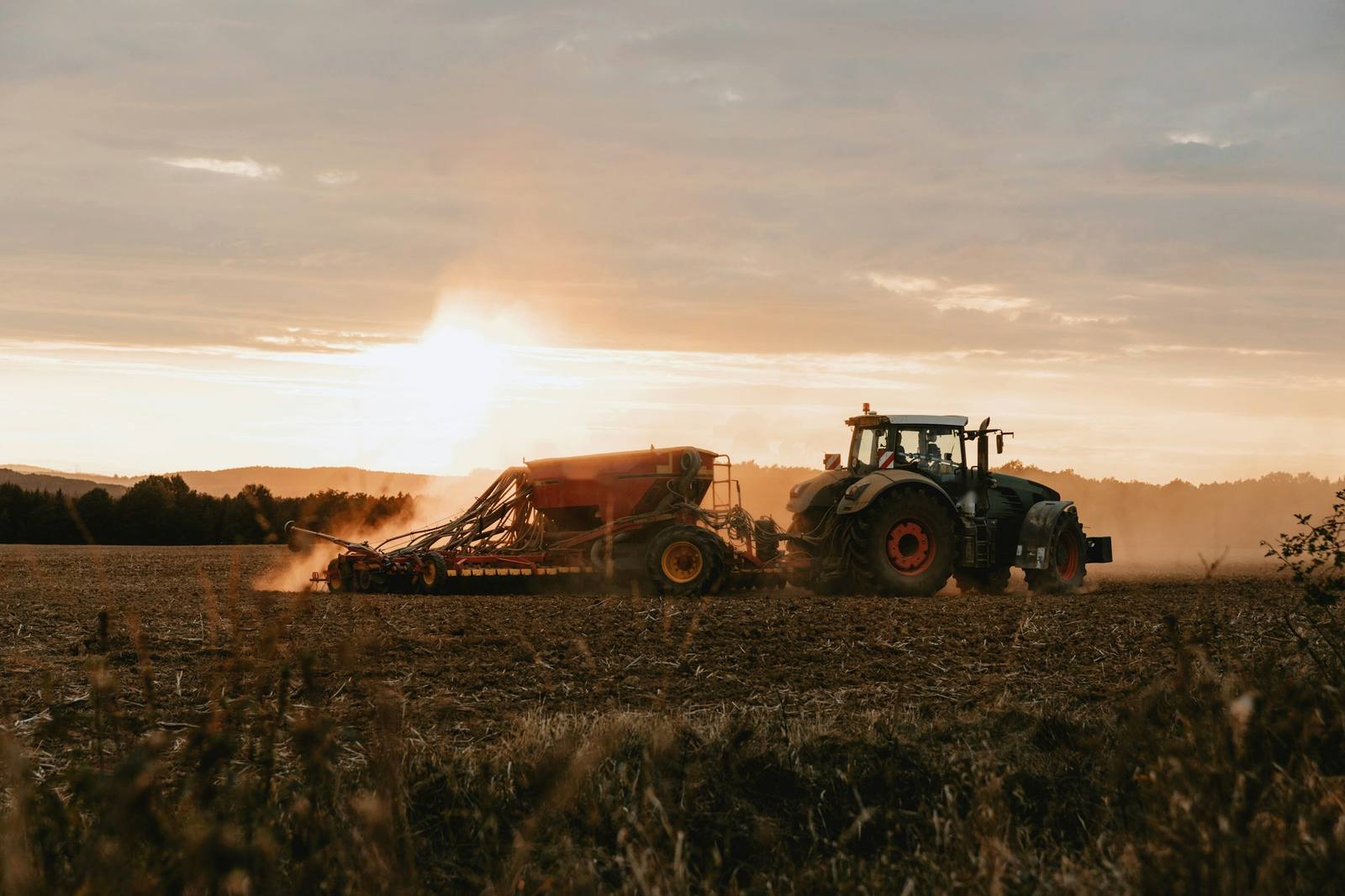 Tractor con sembradora levantando polvo en el campo al atardecer