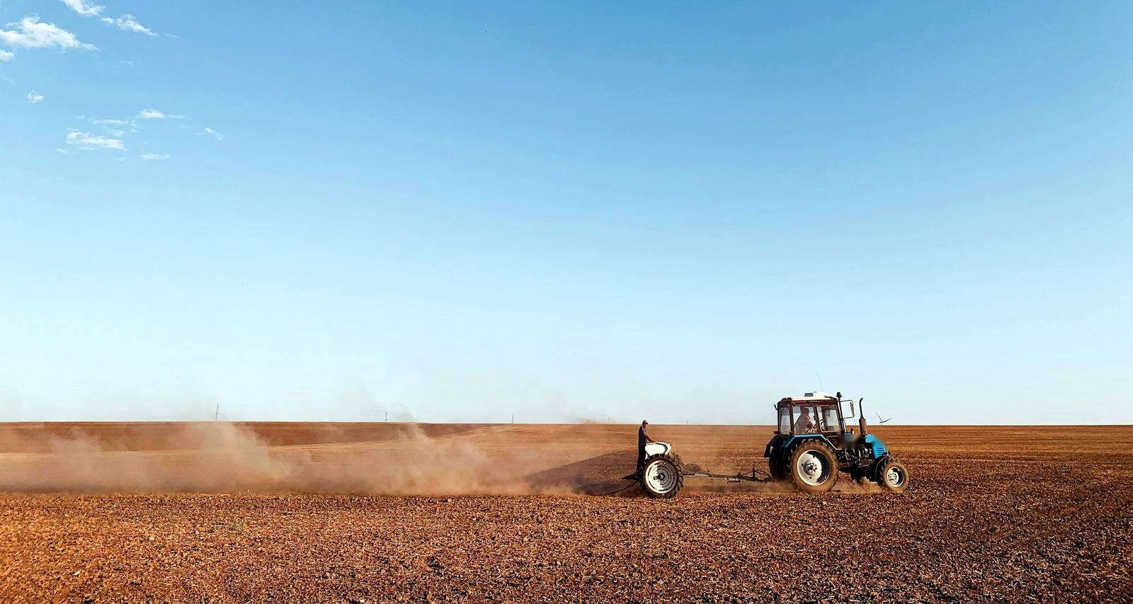 Tractor agrícola sembrando un campo seco a pleno sol, levantando polvo