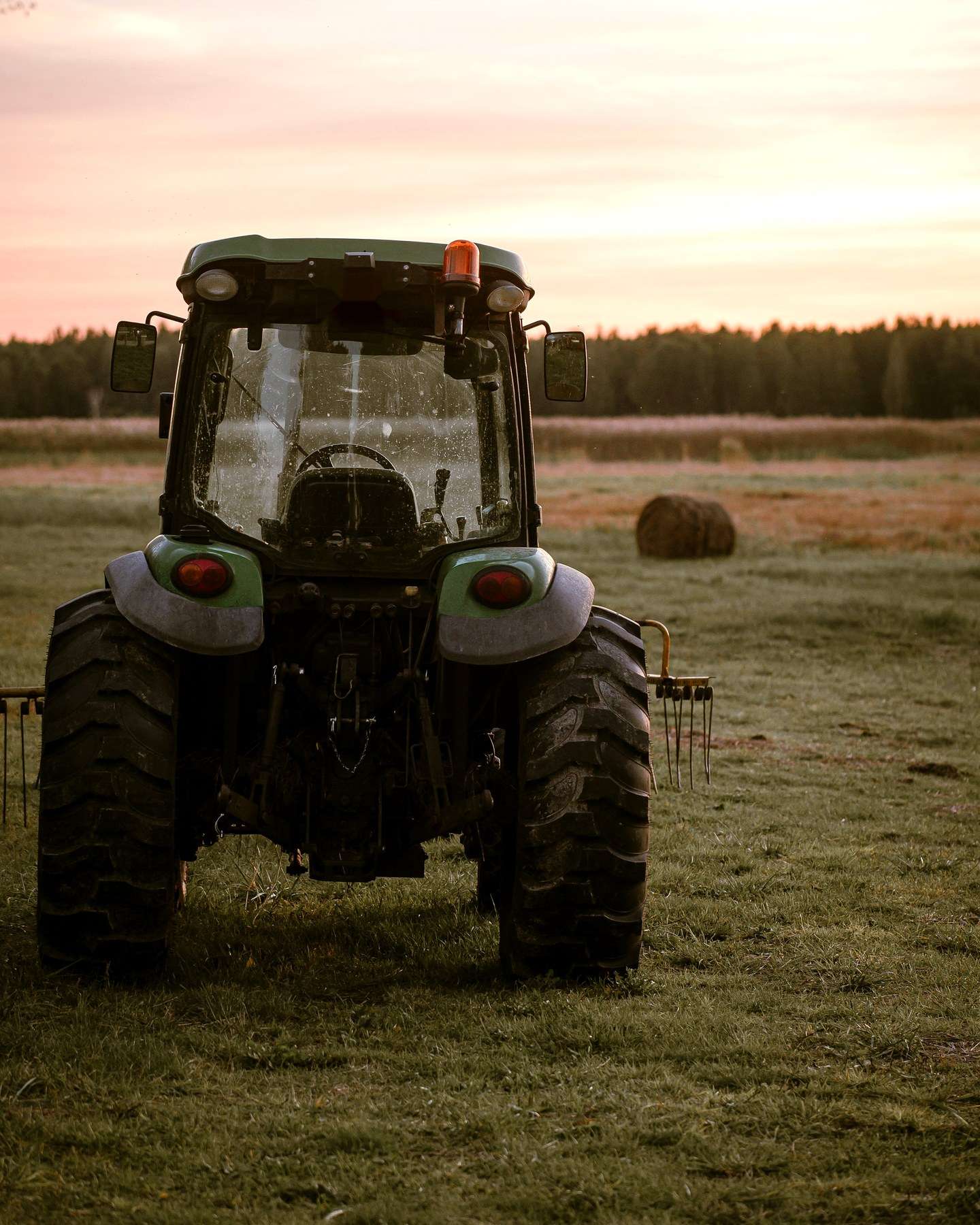 Tractor agrícola en un potrero al amanecer, con pacas de heno al fondo